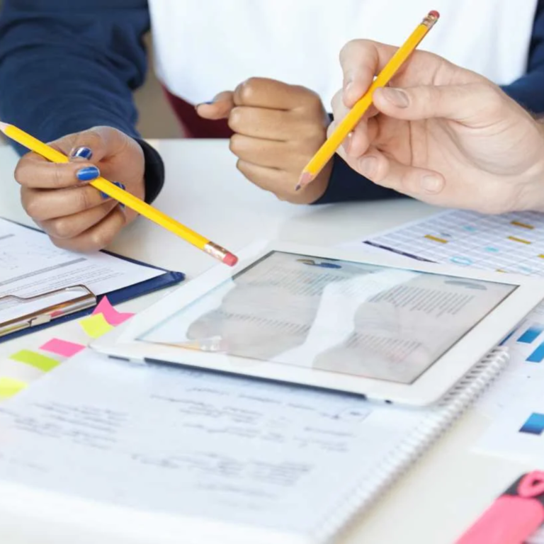 Dos personas revisan documentos y gráficas con lápiz y tableta sobre una mesa de trabajo