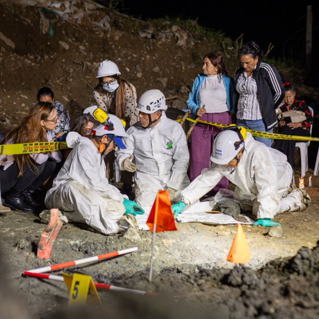 Equipo forense con trajes blancos y cascos excava de noche en La Escombrera mientras familiares observan tras la cinta de peligro